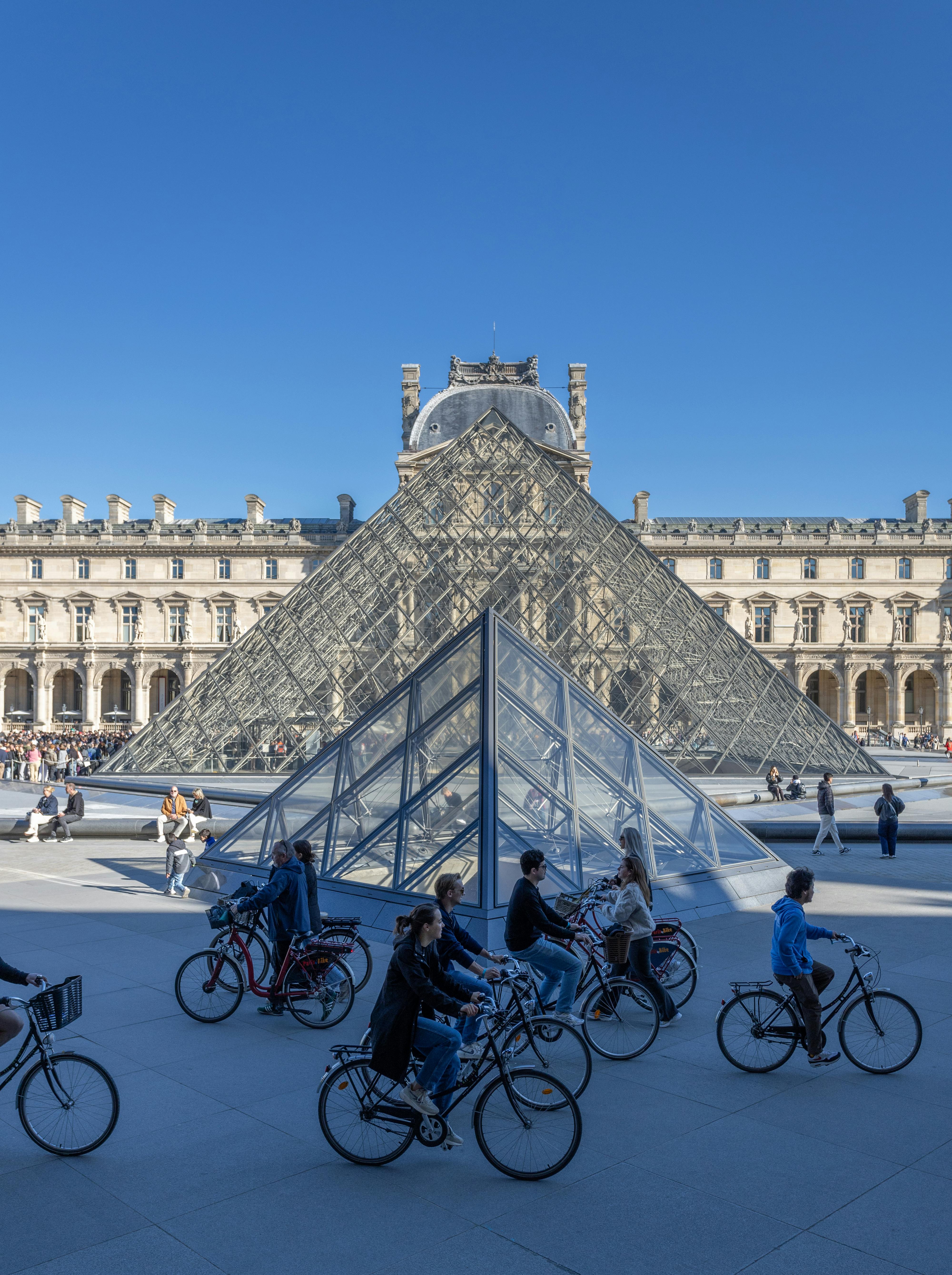 People riding bicycles near the Louvre Pyramids